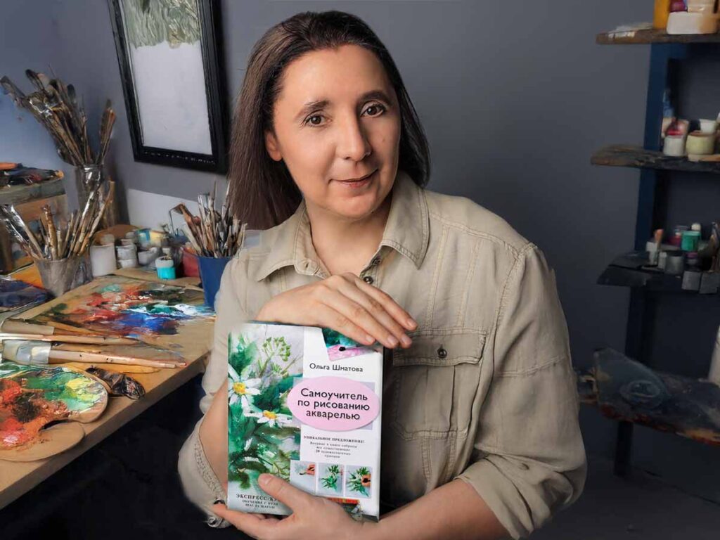 Olga Shmatova holding bestselling watercolor tutorial book in art studio